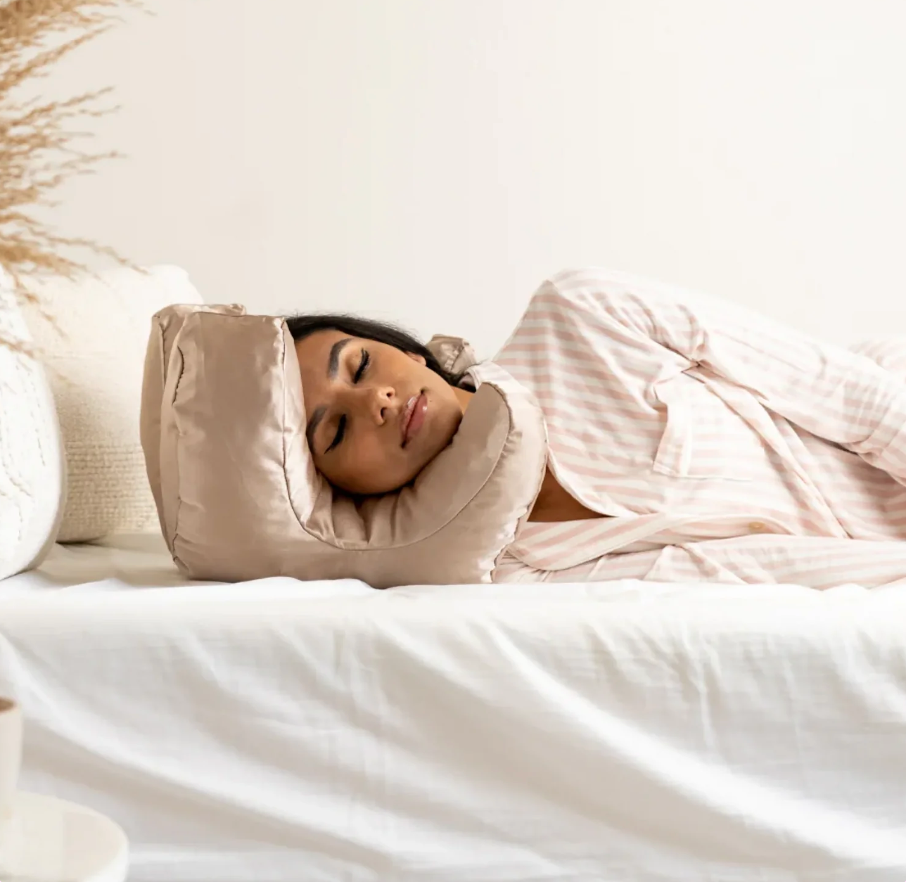 Woman sleeping comfortably on a beige Beauty Sleep Pillow by getblissyneck lying on a white bed