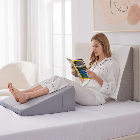 Woman in pajamas reading on bed with gray Bed Wedge Pillow supporting her legs and back