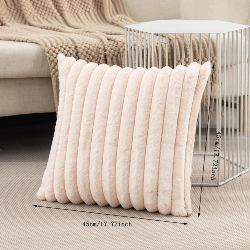 Beige fluffy throw pillow with soft ribbed texture placed on carpet next to metal side table