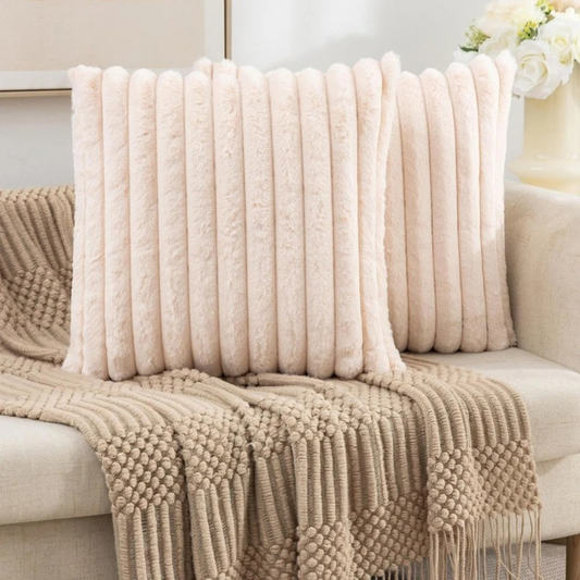 Soft cream colored fluffy throw pillow with vertical ribbed texture on beige couch with knitted throw blanket