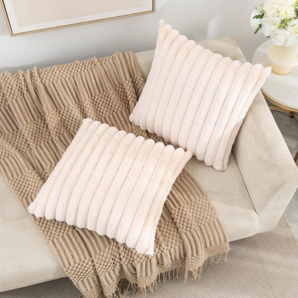 Two beige fluffy throw pillows with ribbed texture on a beige couch with a textured brown throw blanket