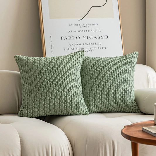 Set of two green knitted throw pillows case on a beige sofa with modern art in the background