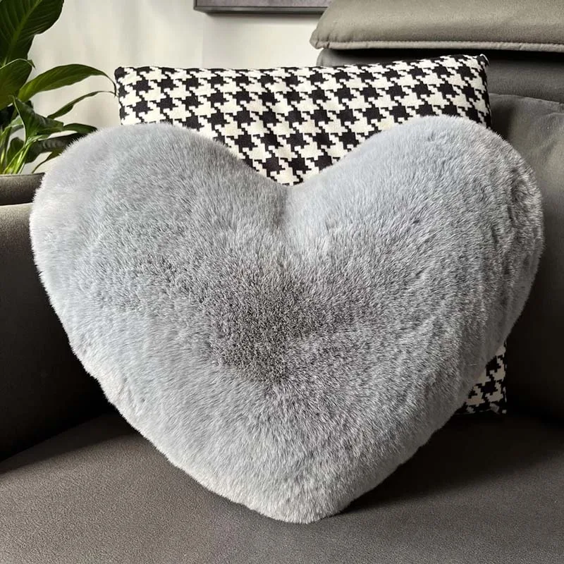Soft gray heart-shaped Throw Pillow with plush fur texture on dark couch with patterned pillow