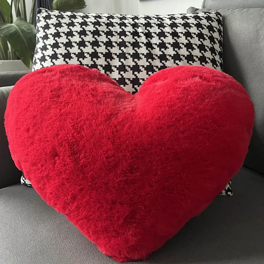Red heart-shaped fluffy throw pillow in front of black and white houndstooth patterned throw pillow on gray couch