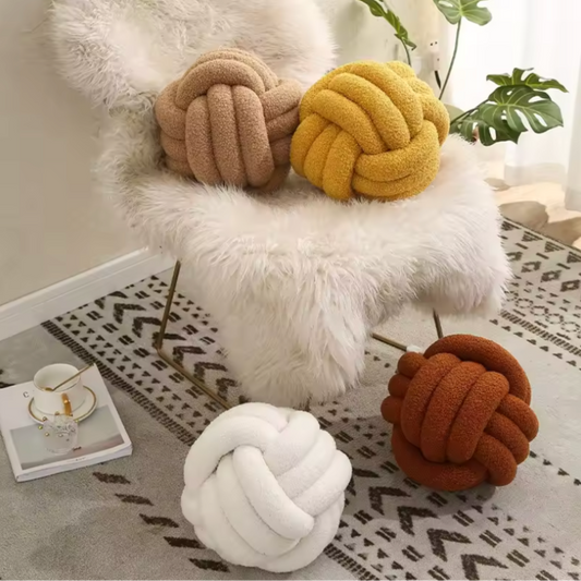 getblissyneck Knot Plush Pillow in white, brown, yellow, and rust colors on a white fur chair and floor