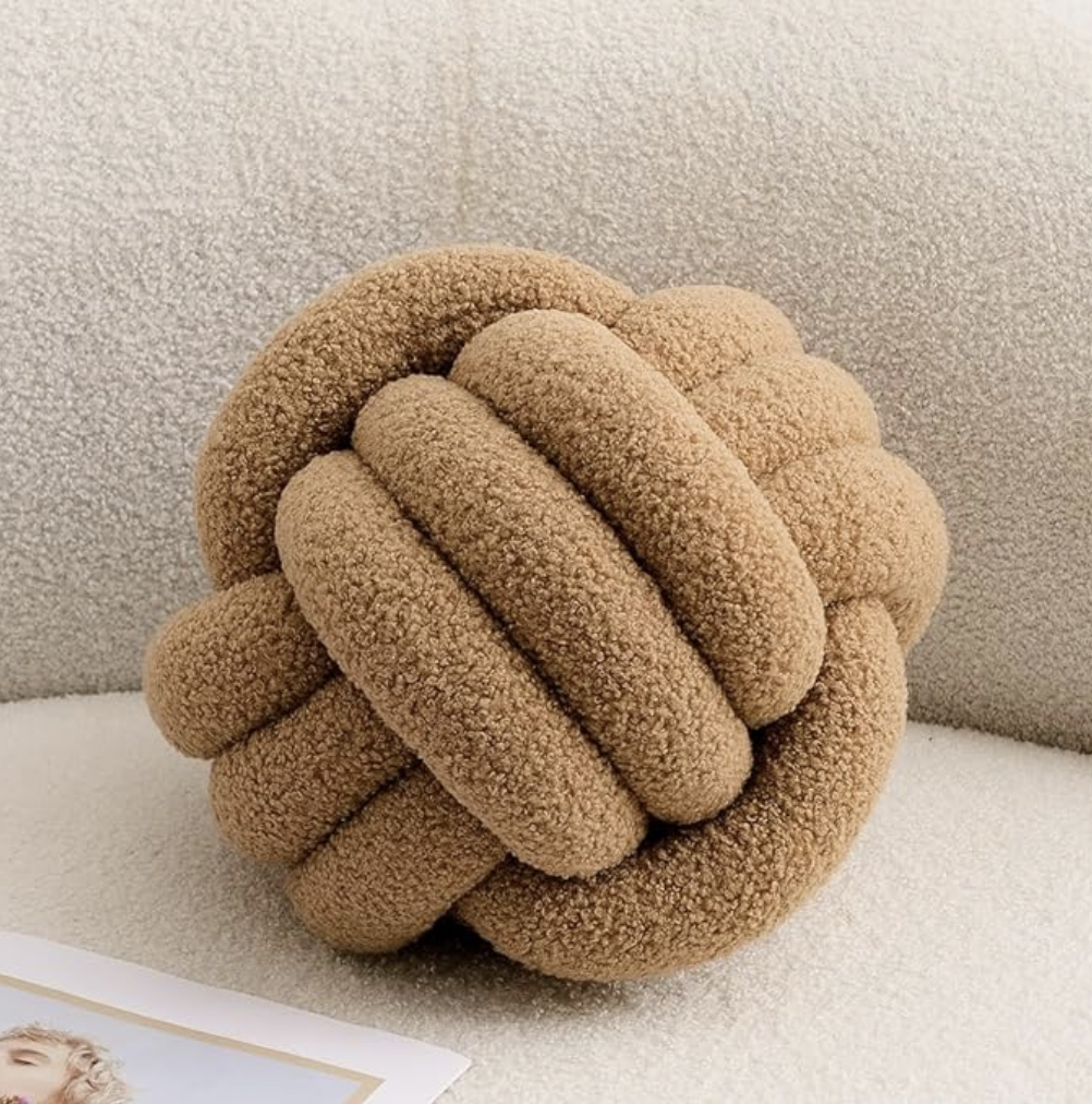 Cozy brown Knot Plush Pillow made of soft textured fabric displayed on a cream sofa