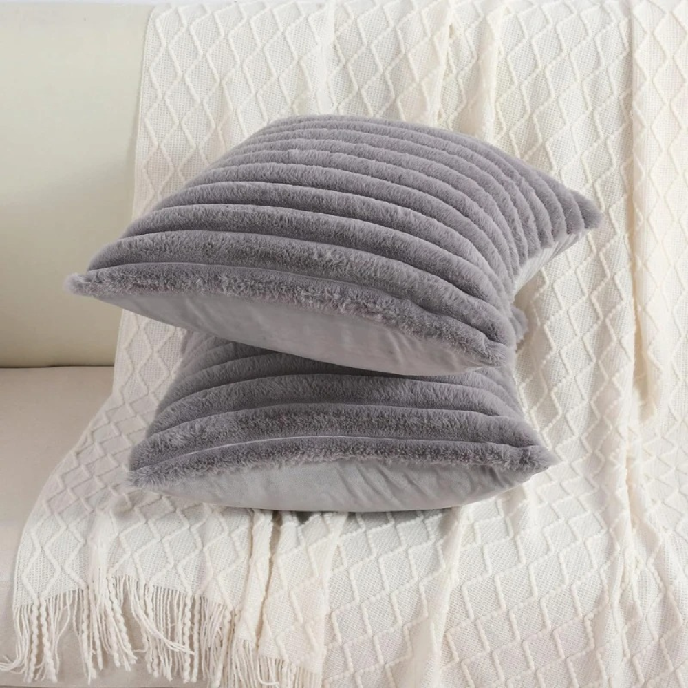 Soft grey throw pillow grey case with ribbed texture placed on a white knitted blanket on sofa