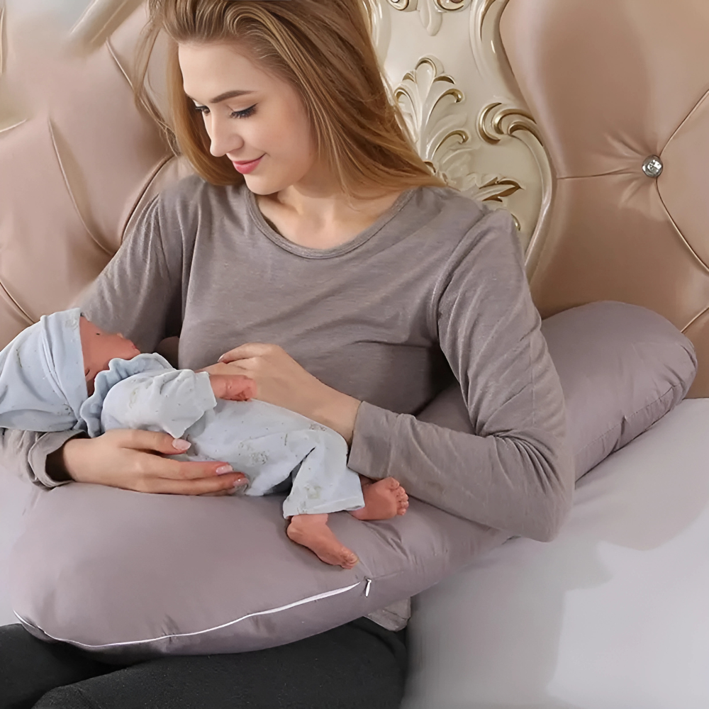 Mother holding baby while sitting with gray Body Shaped Pregnancy Pillow for support