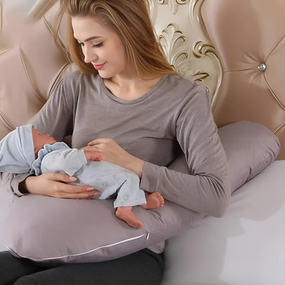 Mother holding baby while sitting with gray Body Shaped Pregnancy Pillow for support